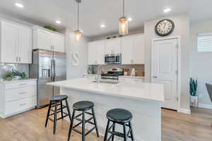 Kitchen featuring white cabinetry, appliances with stainless steel finishes, decorative light fixtures, and sink