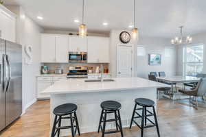 Kitchen featuring sink, white cabinetry, hanging light fixtures, appliances with stainless steel finishes, and a kitchen island with sink