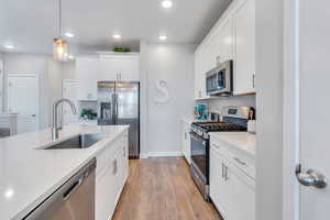 Kitchen featuring pendant lighting, sink, white cabinets, decorative backsplash, and stainless steel appliances