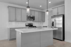 Kitchen featuring appliances with stainless steel finishes, sink, hanging light fixtures, and a center island with sink