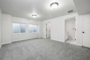 Unfurnished bedroom with ensuite bath, light colored carpet, and a textured ceiling