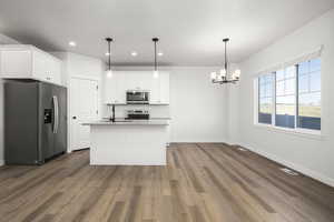 Kitchen with white cabinetry, wood-type flooring, an island with sink, hanging light fixtures, and stainless steel appliances