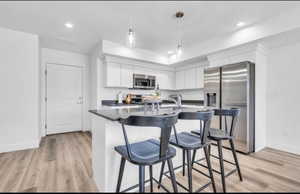 Kitchen featuring a breakfast bar, white cabinetry, hanging light fixtures, light wood-type flooring, and appliances with stainless steel finishes