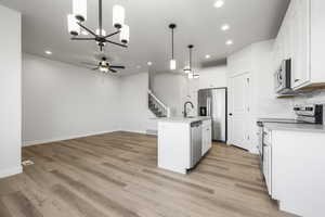 Kitchen featuring sink, appliances with stainless steel finishes, a kitchen island with sink, hanging light fixtures, and white cabinets