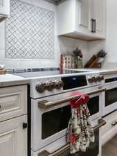 Kitchen featuring backsplash, white cabinets, and high end range