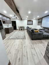 Living room with beamed ceiling, sink, and light wood-type flooring