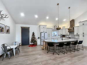 Kitchen featuring hanging light fixtures, vaulted ceiling, high end white fridge, and a spacious island