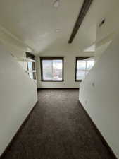 Spare room with lofted ceiling with beams and dark colored carpet