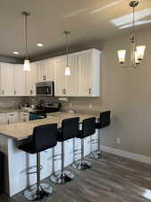 Kitchen with a breakfast bar area, stainless steel appliances, white cabinets, decorative light fixtures, and kitchen peninsula