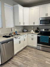 Kitchen featuring sink, white cabinetry, light stone counters, light wood-type flooring, and appliances with stainless steel finishes