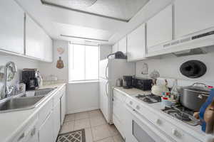 Kitchen featuring white cabinetry, sink, light tile patterned floors, and white appliances