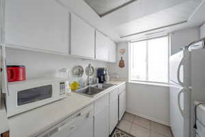 Kitchen featuring light tile patterned flooring, sink, white cabinets, and white appliances