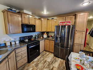 Kitchen featuring sink, light hardwood / wood-style floors, a textured ceiling, and black appliances