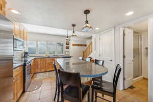 Kitchen featuring decorative light fixtures, light tile patterned flooring, stainless steel appliances, and a kitchen bar