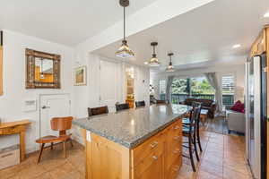 Kitchen with a breakfast bar, a center island, hanging light fixtures, light tile patterned floors, and stainless steel fridge