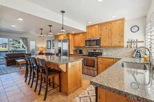 Kitchen featuring appliances with stainless steel finishes, a breakfast bar, sink, decorative backsplash, and hanging light fixtures