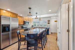 Kitchen featuring hanging light fixtures, light tile patterned floors, appliances with stainless steel finishes, a kitchen island, and dark stone counters