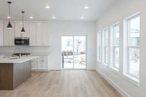 Kitchen featuring tasteful backsplash, white cabinetry, sink, hanging light fixtures, and a center island with sink