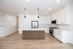 Kitchen featuring appliances with stainless steel finishes, a kitchen island with sink, white cabinets, and backsplash