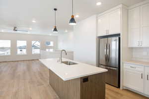 Kitchen with stainless steel refrigerator, white cabinetry, sink, hanging light fixtures, and a center island with sink