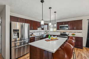 Kitchen with appliances with stainless steel finishes, a center island, pendant lighting, and light wood-type flooring