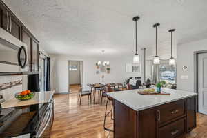 Kitchen with pendant lighting, a kitchen breakfast bar, light hardwood / wood-style floors, dark brown cabinetry, and stainless steel appliances