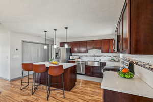 Kitchen featuring a kitchen bar, light wood-type flooring, appliances with stainless steel finishes, a kitchen island, and backsplash