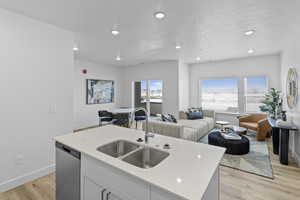 Kitchen with dishwasher, sink, white cabinets, light stone countertops, and a center island with sink