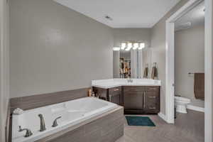 Bathroom featuring vanity, toilet, and tiled tub