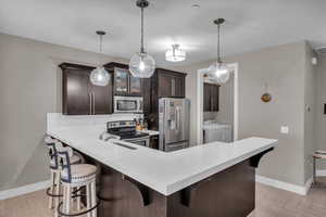 Kitchen featuring light parquet floors, appliances with stainless steel finishes, dark brown cabinets, washer and dryer, and a kitchen bar