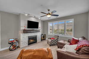 Living room featuring ceiling fan, track lighting, and a stone fireplace