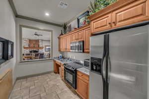 Kitchen featuring sink, light stone counters, ornamental molding, ceiling fan, and stainless steel appliances