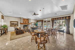 Dining room featuring ceiling fan, a stone fireplace, ornamental molding, and a textured ceiling