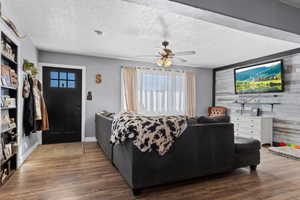 Living room featuring ceiling fan, dark hardwood / wood-style floors, a textured ceiling, and wood walls