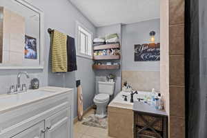 Bathroom featuring vanity, toilet, tiled tub, tile patterned floors, and a textured ceiling