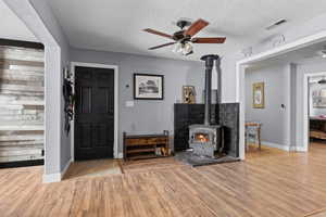 Unfurnished living room featuring ceiling fan, light hardwood / wood-style flooring, a textured ceiling, and a wood stove