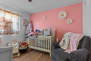 Bedroom featuring a crib, hardwood / wood-style flooring, a textured ceiling, and ceiling fan