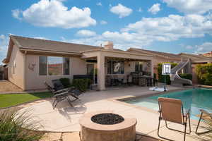 Back of house with stucco siding, an outdoor fire pit, a patio area, exterior kitchen, and an outdoor pool