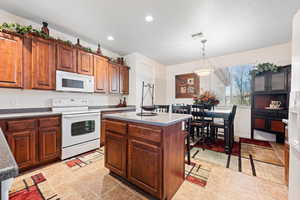 Kitchen with pendant lighting, white appliances, a center island, and light tile patterned flooring