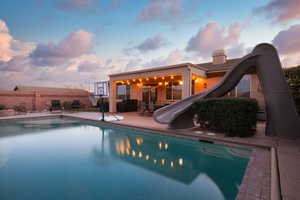 Pool at dusk featuring a patio area, a fenced in pool, fence, and a water slide