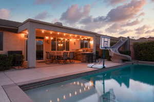 Pool at dusk with an outdoor pool, outdoor dry bar, a water slide, and a patio