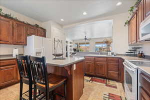 Kitchen with sink, white appliances, a breakfast bar, ceiling fan, and light tile patterned flooring