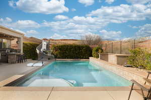 View of pool with outdoor dry bar, area for grilling, a patio area, a water slide, and a fenced backyard