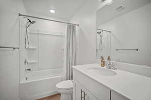 Full bathroom with hardwood / wood-style flooring, vanity, shower / bathtub combination with curtain, and toilet