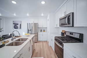 Kitchen featuring sink, white cabinetry, light hardwood / wood-style flooring, stainless steel appliances, and light stone countertops