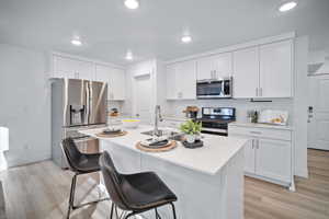 Kitchen featuring white cabinetry, sink, a kitchen island with sink, stainless steel appliances, and light hardwood / wood-style flooring