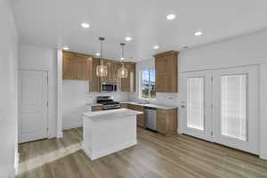 Kitchen with sink, light hardwood / wood-style flooring, a kitchen island, pendant lighting, and stainless steel appliances