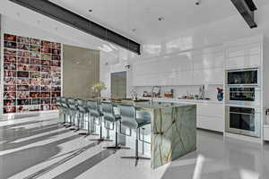 Kitchen with white cabinetry, beam ceiling, a spacious island, built in microwave, and decorative light fixtures