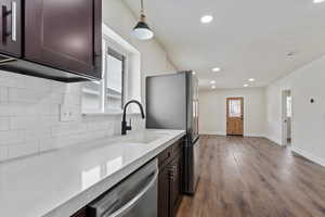 Kitchen with dark brown cabinetry, sink, appliances with stainless steel finishes, pendant lighting, and decorative backsplash