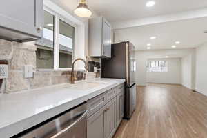 Kitchen featuring stainless steel dishwasher, gray cabinets, sink, and light wood-type flooring